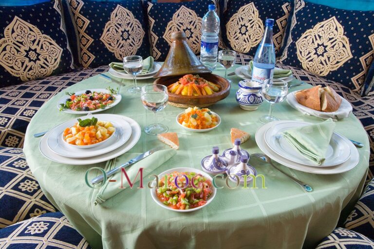 Table de repas, nappe verte, coussins bleus, tajines et salades