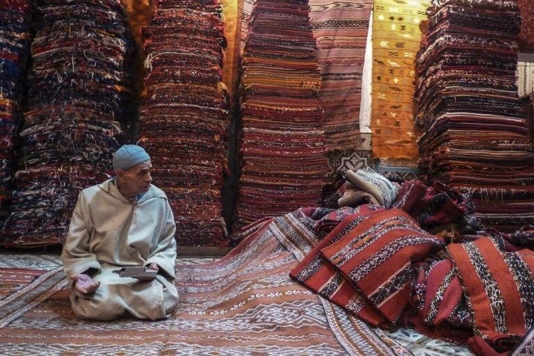 Vendeur de tapis dans sa boutique, avec des piles de tapis et une calculette