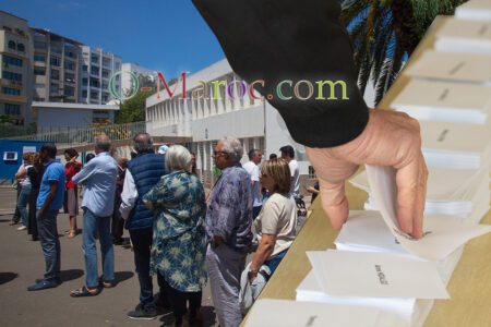 Une main prend un bulletin de vote sur fond d'électeurs au lycée Lyautey